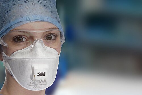 Portrait einer Frau mit Schutzbrille und medizinischer Gesichtsmaske mit 3M-Logo