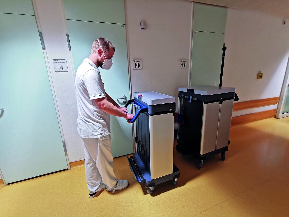 Ein Mitarbeiter in weißer Arbeitskleidung auf einem Flur des Dietrich-Bonhoeffer-Klinikums Neubrandenburg schiebt das abkoppelbare Modul des Vileda Origo 2 Reinigungswagens in Richtung des restlichen Wagens.