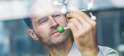 Ein Mann der das Modell eines Moleküls vor sein Gesicht hält und betrachtet
