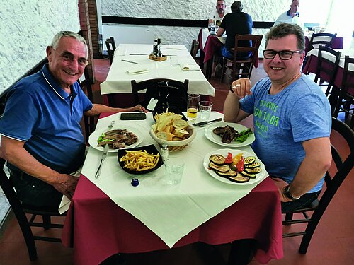 ReinigungsMarkt-Urgestein Gianpaolo Redi und Knittler-Redakteur Mark Schmiechen sitzen an einem Tisch in einem Restaurant und lächeln in die Kamera. Auf dem Tisch stehen verschiedene Speisen.