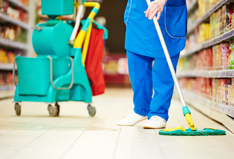 Eine Reinigungskraft wischt mit einem Flachwischer den Boden eines Supermarktes