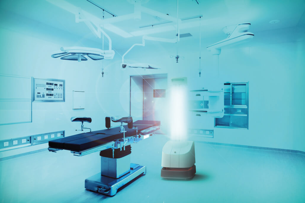 Eine Operationsliege in einem OP-Saal. Daneben steht ein hell leuchtender UV-C-Roboter. Das Bild ist in türkis-blaues Licht getaucht.
