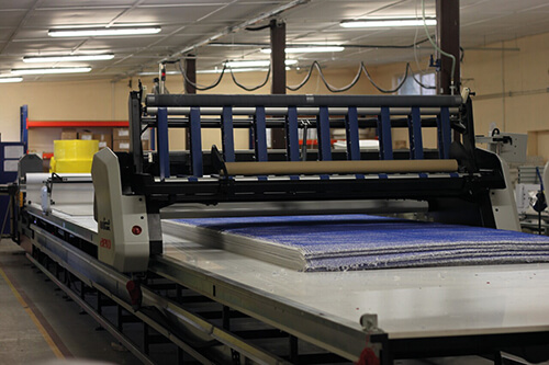 Eine Maschine, in der große blaue Stoffbahnen für die Produktion von Mopptex Wischtextilien liegen