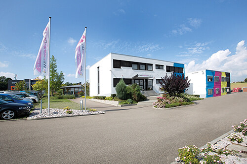 Außenansicht des Firmengebäudes von WIRmachenDRUCK. Ein Teil der Fassade ist in Cyan, Magenta, Gelb und Schwarz gesctrichen.